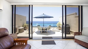 A balcony with a table, chairs, and an umbrella, overlooking the sea.