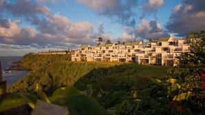 A coastal hotel with multiple-story buildings, a grassy lawn, and a view of the ocean.
