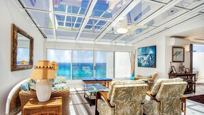 A spacious living room with a large glass ceiling, wicker furniture, and a view of the ocean.