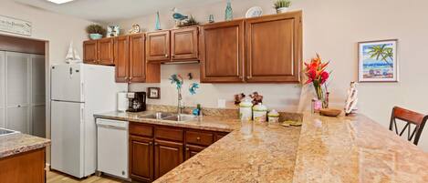 A kitchen with wooden cabinets, a granite countertop, a dishwasher, and a coffee maker.