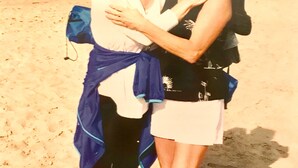 Twee personen staan op een zandstrand, met de oceaan op de achtergrond.