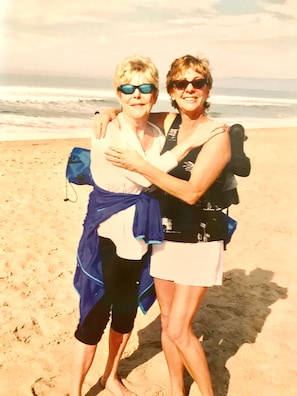 Twee personen staan op een zandstrand, met de oceaan op de achtergrond.