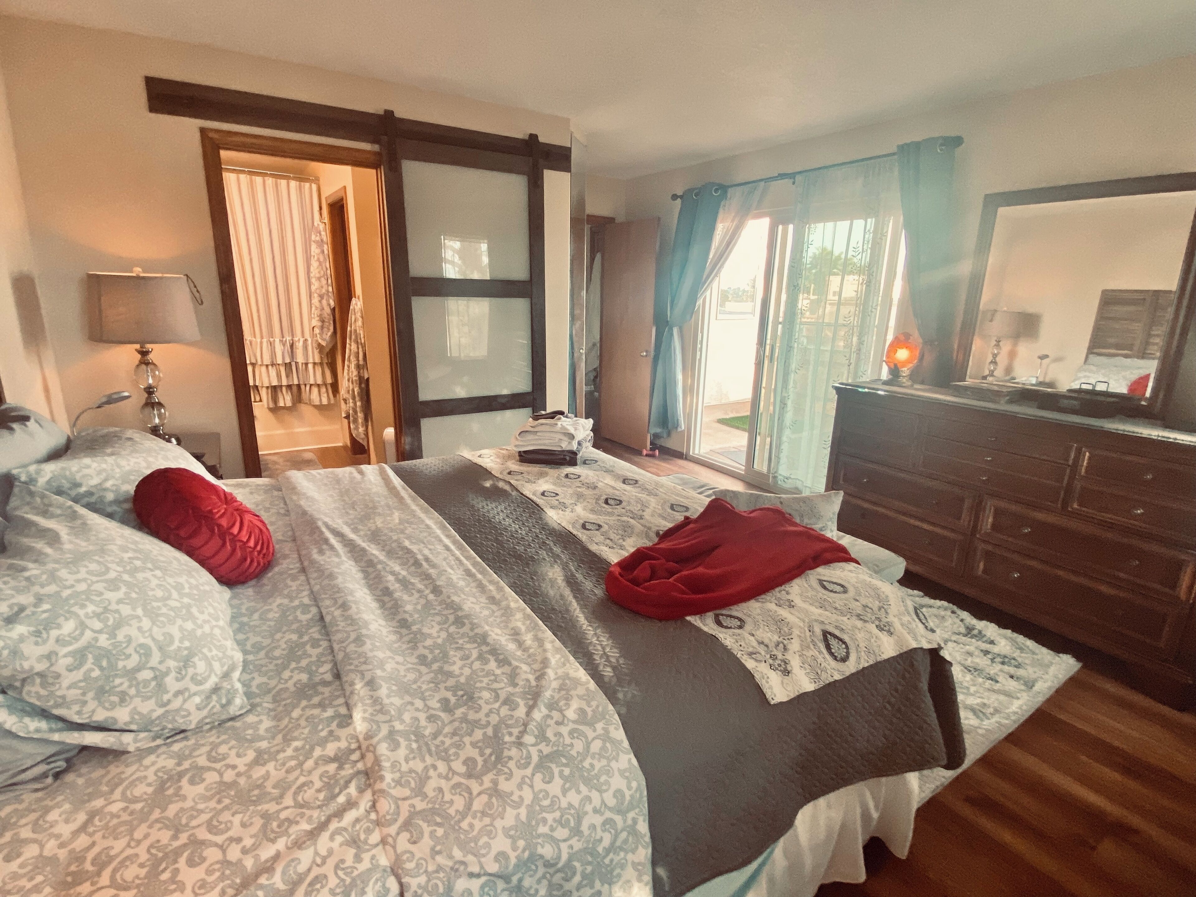Une chambre à coucher comprenant un lit, une commode, une lampe et une porte-fenêtre coulissante donnant sur un balcon.