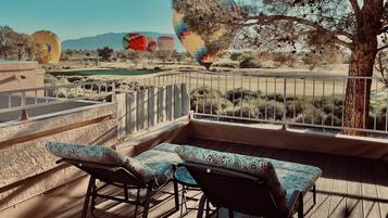 Un balcon agrémenté de deux fauteuils de jardin à motifs, offrant une vue sur des montgolfières et un paysage désertique à la végétation clairsemée.