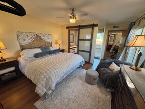 Une chambre à coucher avec un lit, des tables de chevet, une lampe, un ventilateur de plafond et une vue sur l’extérieur.