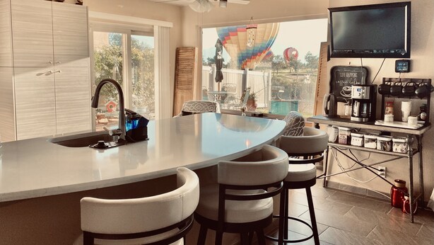 A kitchen with a large island, bar stools, a TV mounted above the counter, and a view of the outdoors. - Golf Course, Mnt Views, Balloons, King Bed, Veranda, Yard, 3 BD, WIFI, BBQ, WD (Albuquerque)