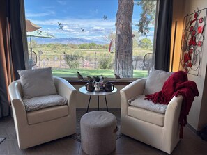 Una habitación con dos sofás orientados hacia una ventana, una pequeña mesa con bebidas y vistas a un árbol y montañas.