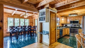 A wooden cabin interior with a dining area, kitchen, and large windows. - Gorgeous Lakefront Log Home w/ Pool & Boat Dock on 3 Fenced Acres! Dogs Welcomed (Harriman)