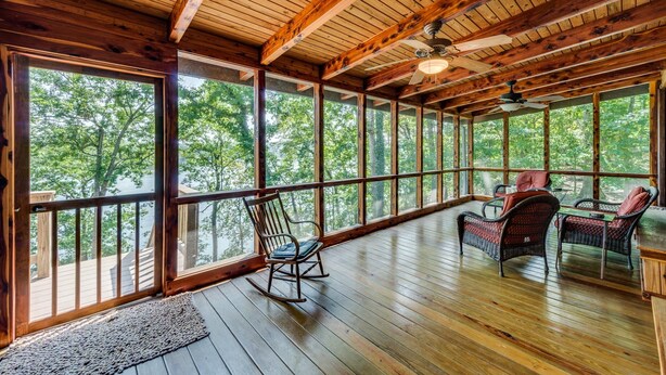 A wooden deck with a rocking chair and wicker furniture, large windows offering a view of trees. - Gorgeous Lakefront Log Home w/ Pool & Boat Dock on 3 Fenced Acres! Dogs Welcomed (Harriman)
