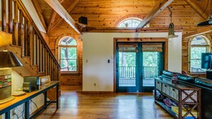 A wooden interior with a staircase, a door leading outside, and a seating area with a table and books. - Gorgeous Lakefront Log Home w/ Pool & Boat Dock on 3 Fenced Acres! Dogs Welcomed (Harriman)
