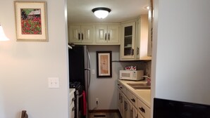 A narrow kitchen with light-colored cabinets, a microwave, and a sink.