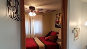 A bedroom with a bed, a ceiling fan, a window with curtains, and a painting on the wall.
