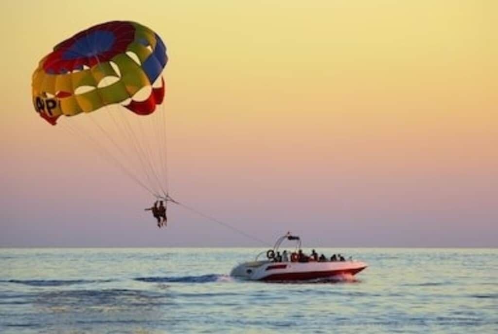 Activitat de parapent sobre l'aigua, amb un vaixell al fons.