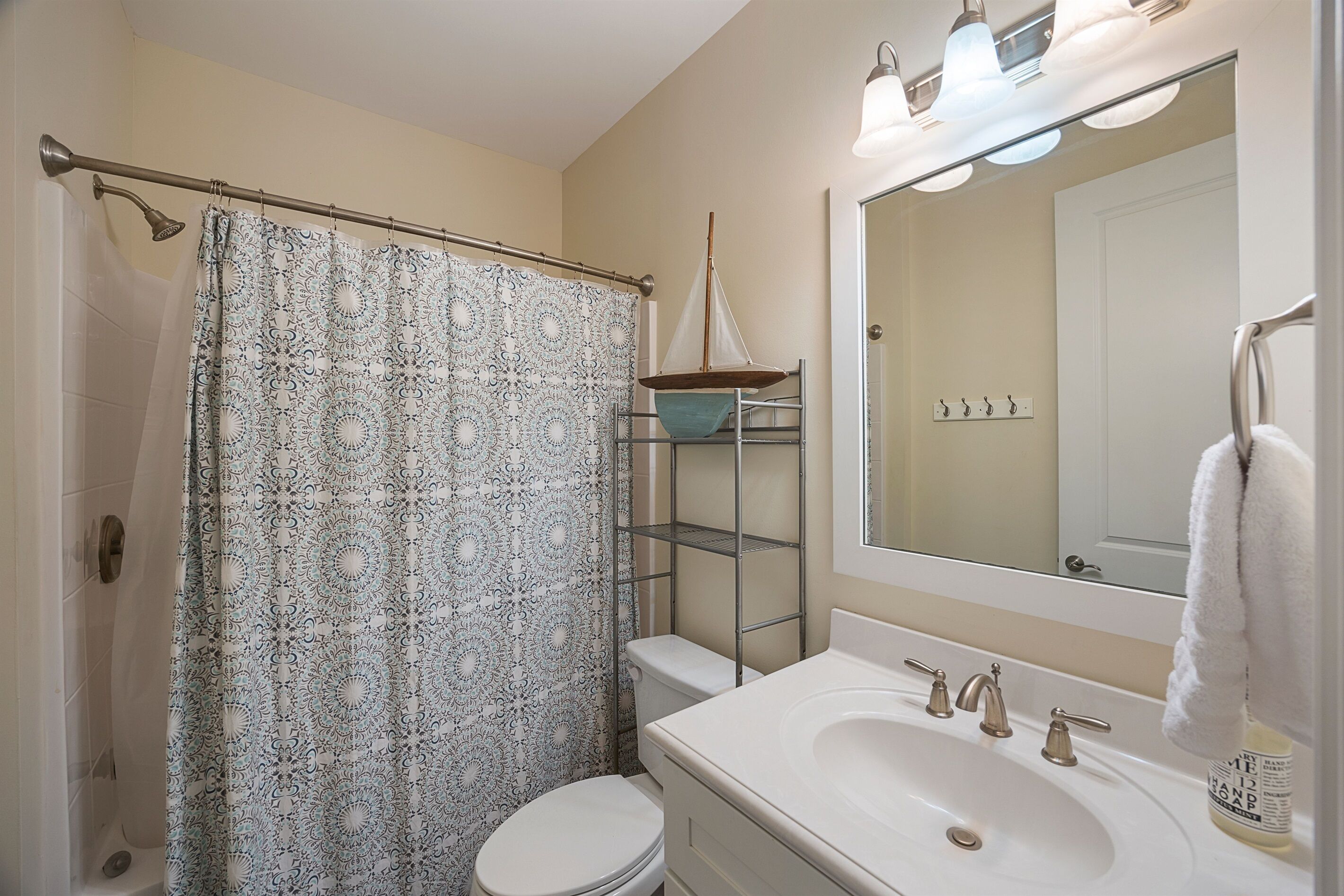 A bathroom with a shower curtain, toilet, sink, and a mirror with a towel rack.
