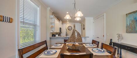 A dining area with a wooden table, chairs, a chandelier, and a view through the window.