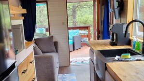 A compact kitchen with wooden cabinets, a countertop, and a sink. There is a window providing natural light and a view of the outdoors.