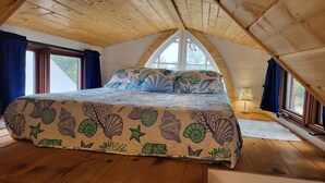A bedroom with a sloped ceiling, a bed with a seashell and leaf patterned bedspread, and a nightstand with a lamp.