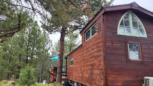 A wooden cabin with a steep roof, large windows, and a small porch area.