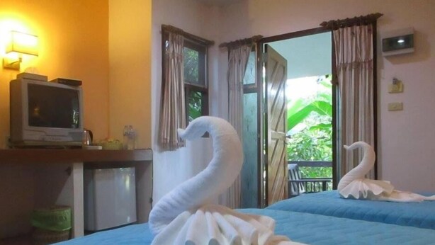Ein Hotelzimmer mit zwei Betten, einem Fernseher auf einem Schreibtisch und einem Balkon mit Vorhängen.