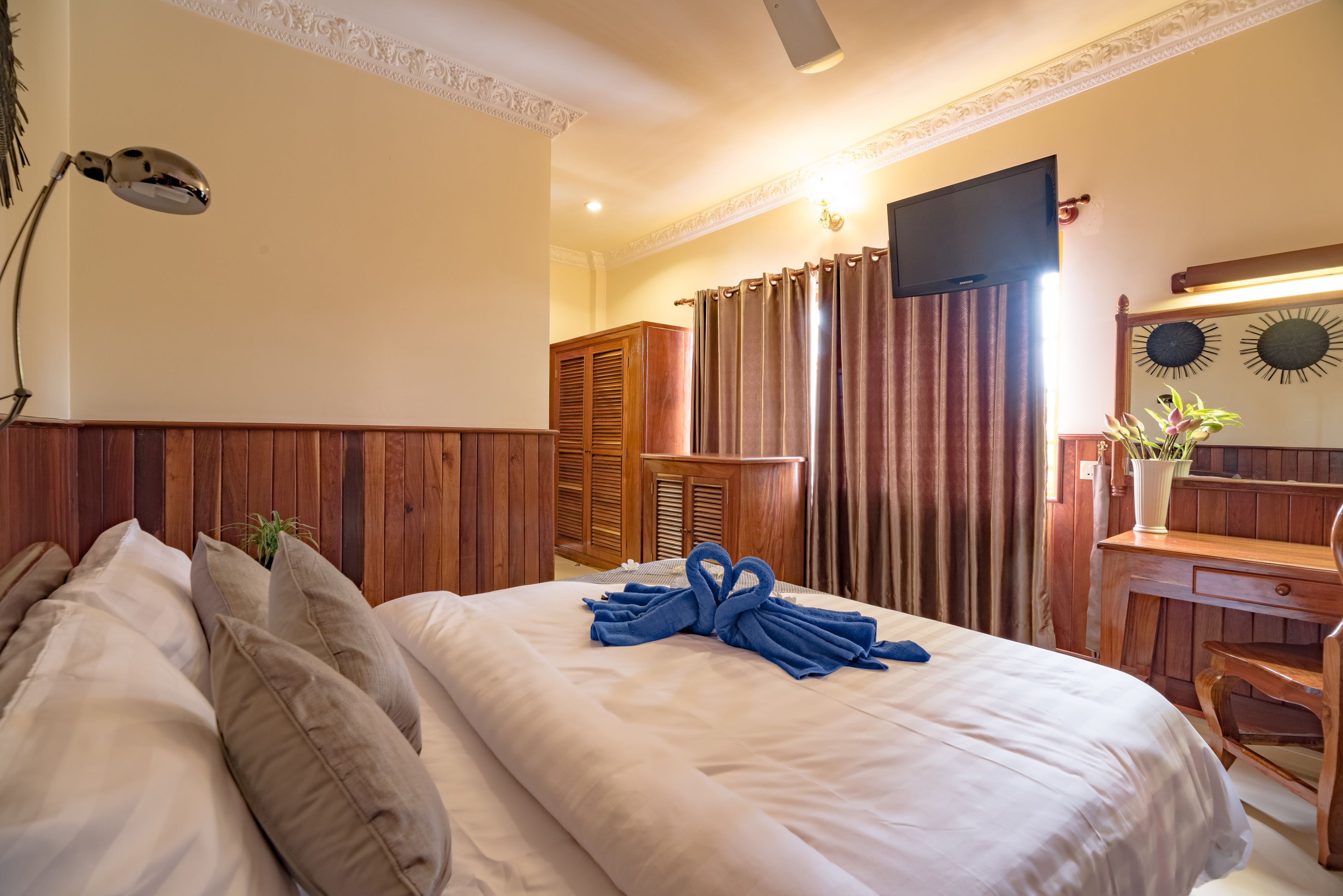 A hotel room with a large bed, wooden headboard, a desk, and a TV mounted on the wall.