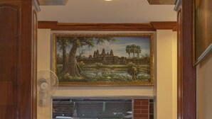 A reception area with a wooden bench, a potted plant, and a framed painting above a window. - The Siem Reap Chilled Backpacker (Siem Reap)
