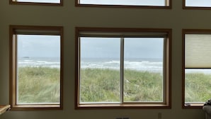 Habitación con tres ventanas que dan a una playa con olas y césped.