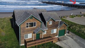 Une maison en bois avec un toit vert et une terrasse, située près d’une côte rocheuse, avec la rivière Coquille visible au loin.