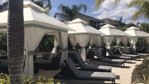 A poolside area with lounge chairs and umbrellas, surrounded by palm trees.
