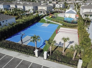 Zona residencial con una cancha de baloncesto azul, rodeada de casas y palmeras.