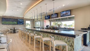 A modern bar area with a curved ceiling, bar stools, a counter with a glass top, and large screens on the wall.