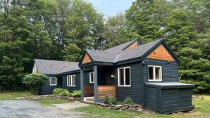 A two-story house with a dark exterior, a front porch, and a stone foundation. - Perfectly located on the Mountain rd between Stowe village and Stowe Mountain (Stowe)