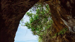 Une formation rocheuse naturelle dotée d’une entrée de grotte, d’une plage de sable et de vagues déferlantes sur l’océan.