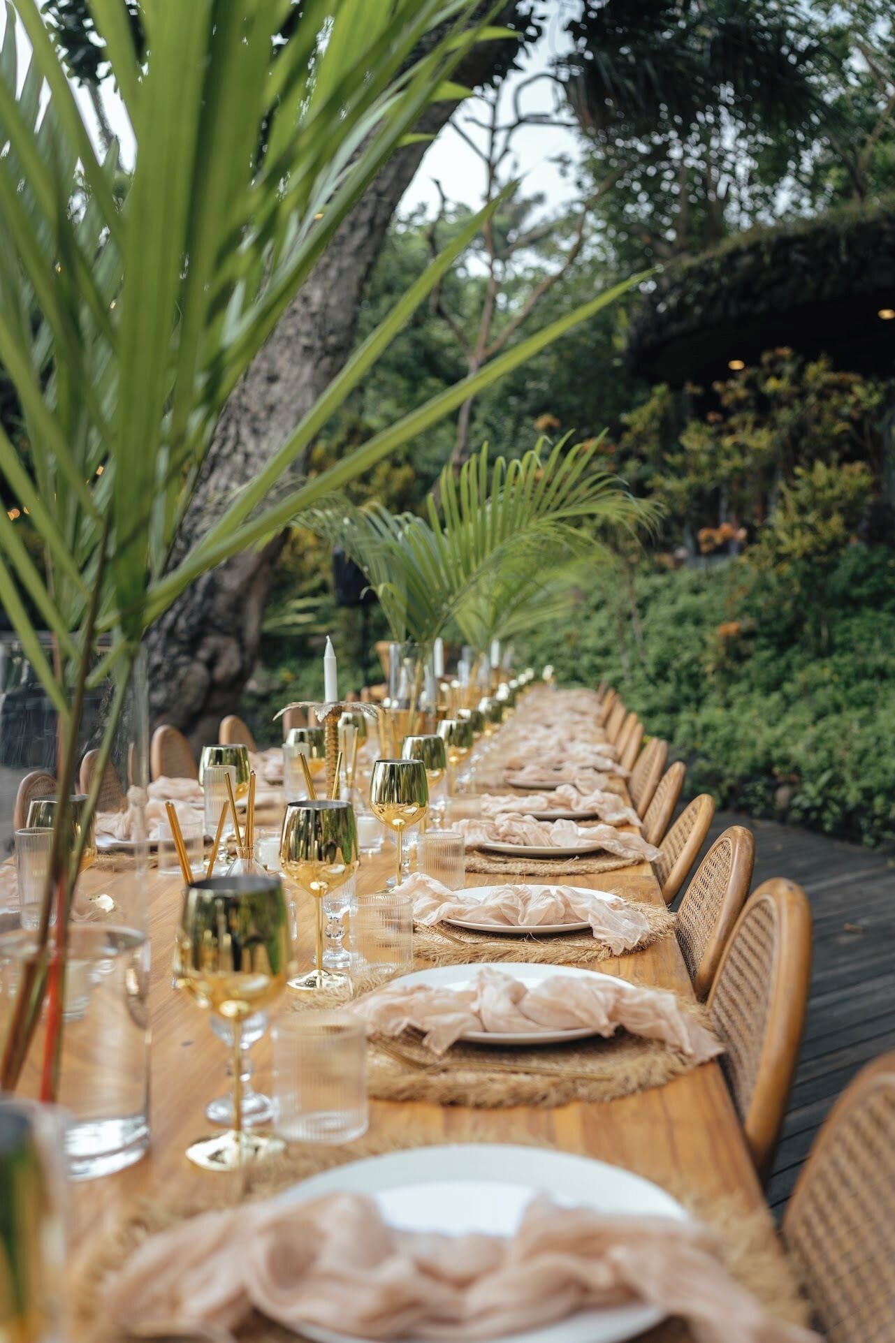 A long dining table set outdoors with chairs, glasses, and plates.