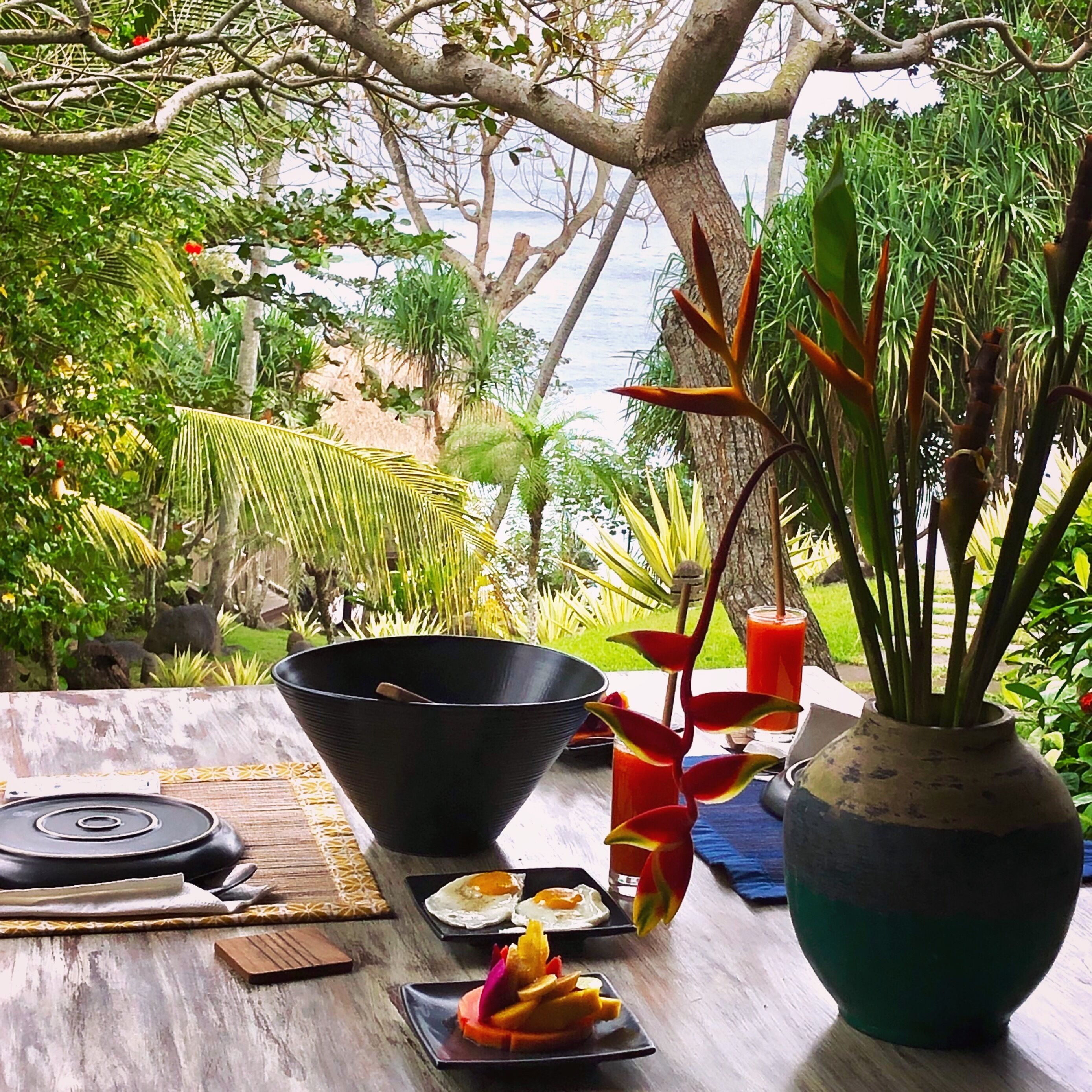 A table with a black bowl, a glass of red drink, and a fruit plate with slices of orange and mango.
