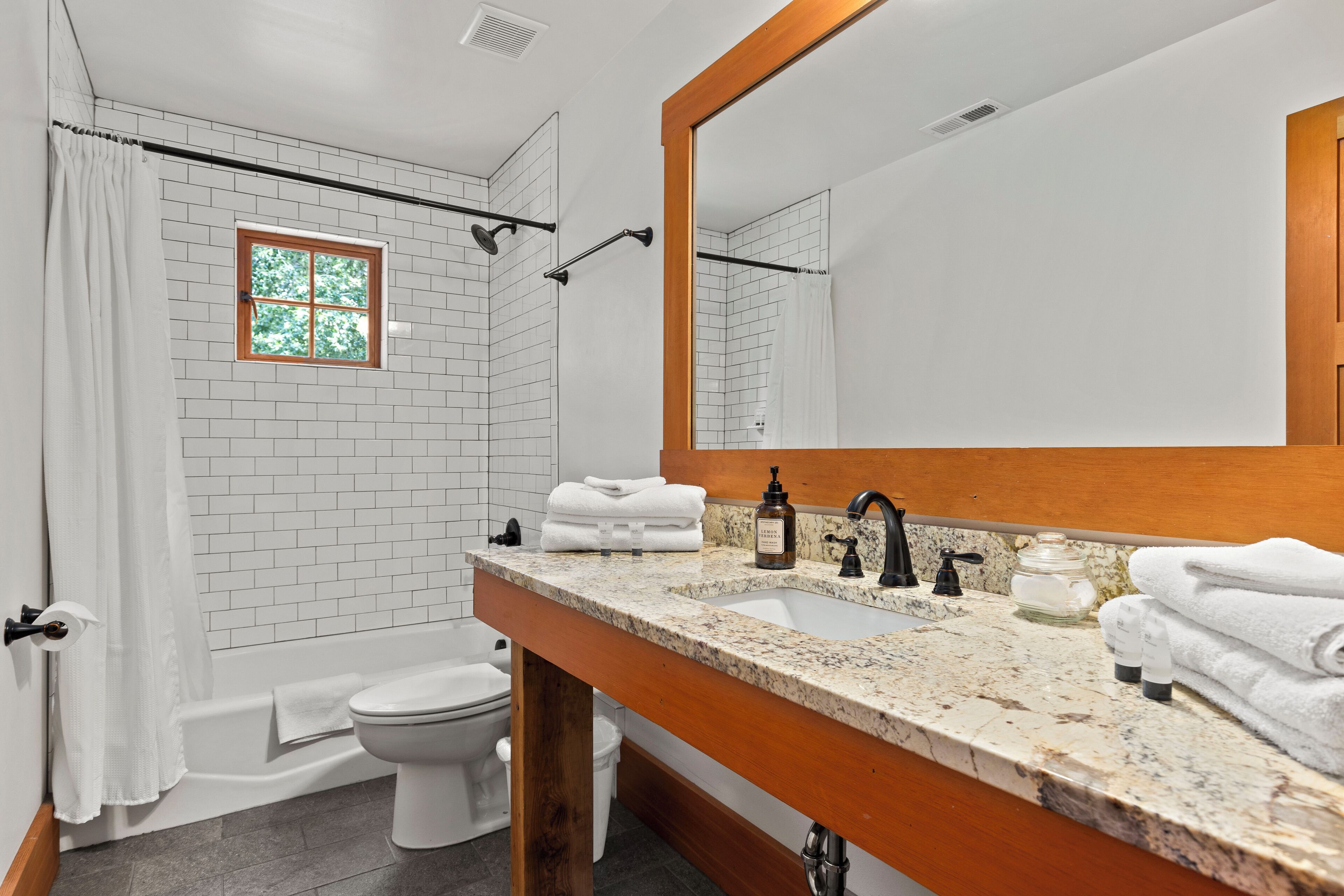 A bathroom with a shower, toilet, sink, and a large mirror.