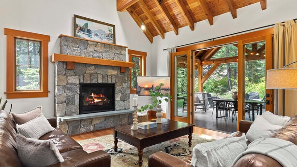 A cozy living room with a stone fireplace, leather furniture, and large windows overlooking a garden. - Suncadia Retreat • 3 porches • Quiet Cul-de-Sac • Fire pit • Bikes (Cle Elum)