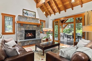 A cozy living room with a stone fireplace, leather furniture, and large windows overlooking a garden. - Suncadia Retreat • half acre • 3 porches • Quiet Cul-de-Sac • Fire pit • Bikes (Cle Elum)