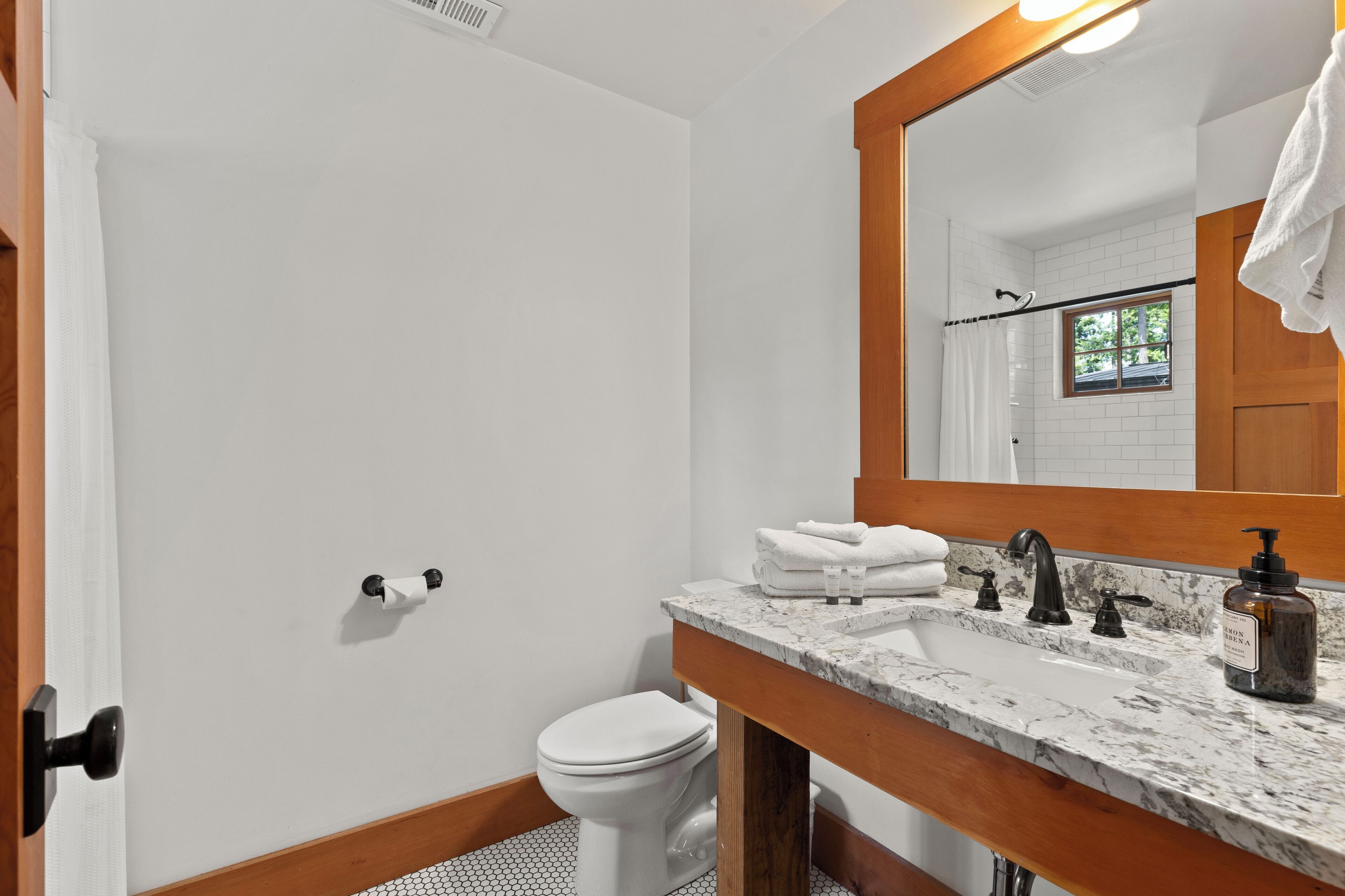 A bathroom with a white toilet, a sink with a marble countertop, a wooden door frame, and a mirror with a wooden frame.