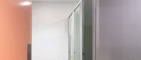 A corridor with glass partitions and a white floor, leading to a room with a door.