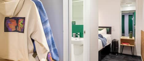 A hotel room with a bed, a desk with a laptop, a suitcase, and a small table with a green water bottle.