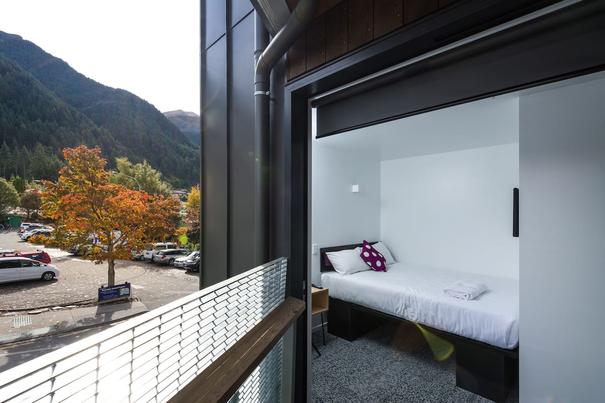 Ein modernes Zimmer mit Bett und Fenster mit Blick auf einen Parkplatz und Berge.