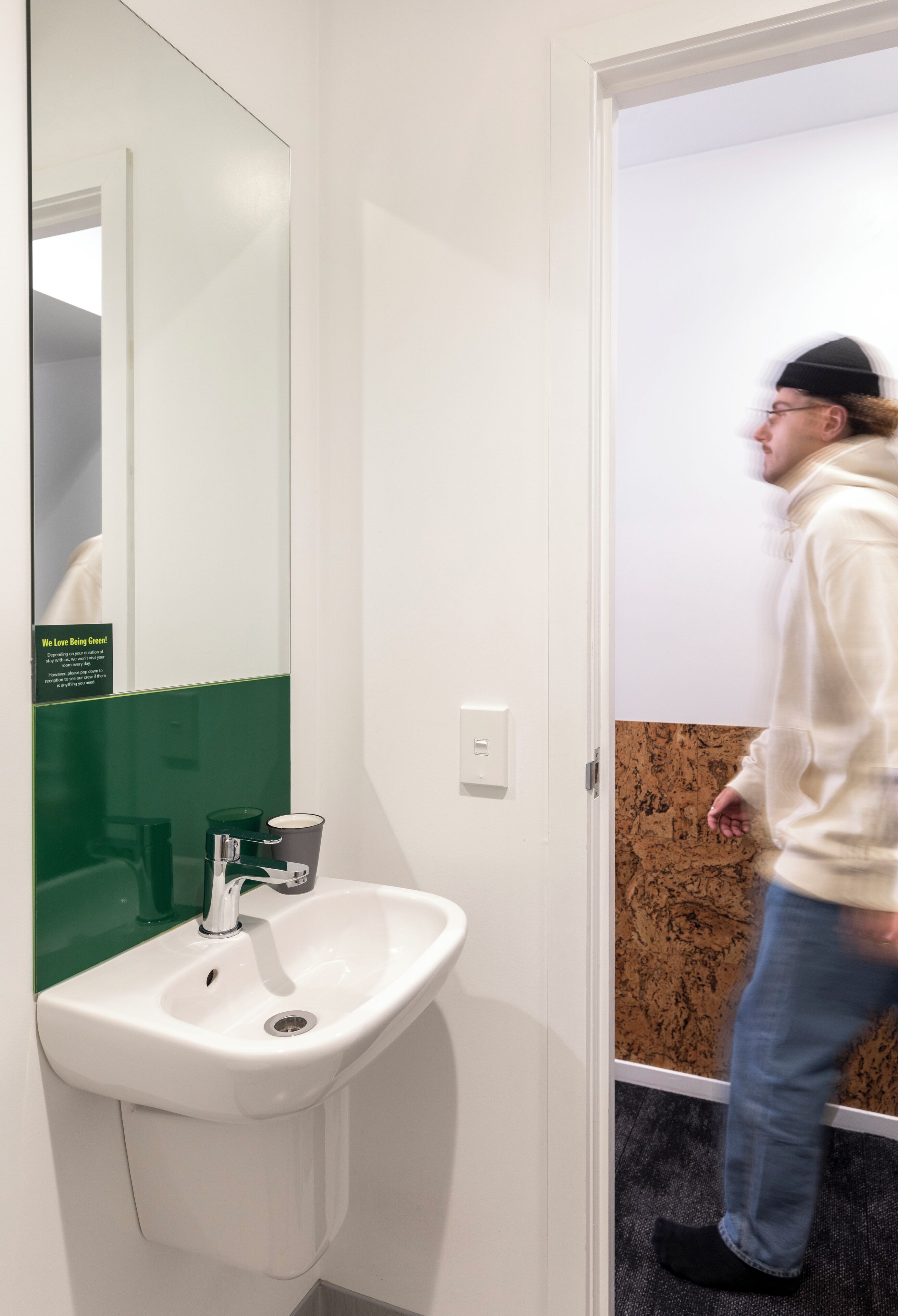A bathroom with a white sink, a green-tiled wall, and a mirror.