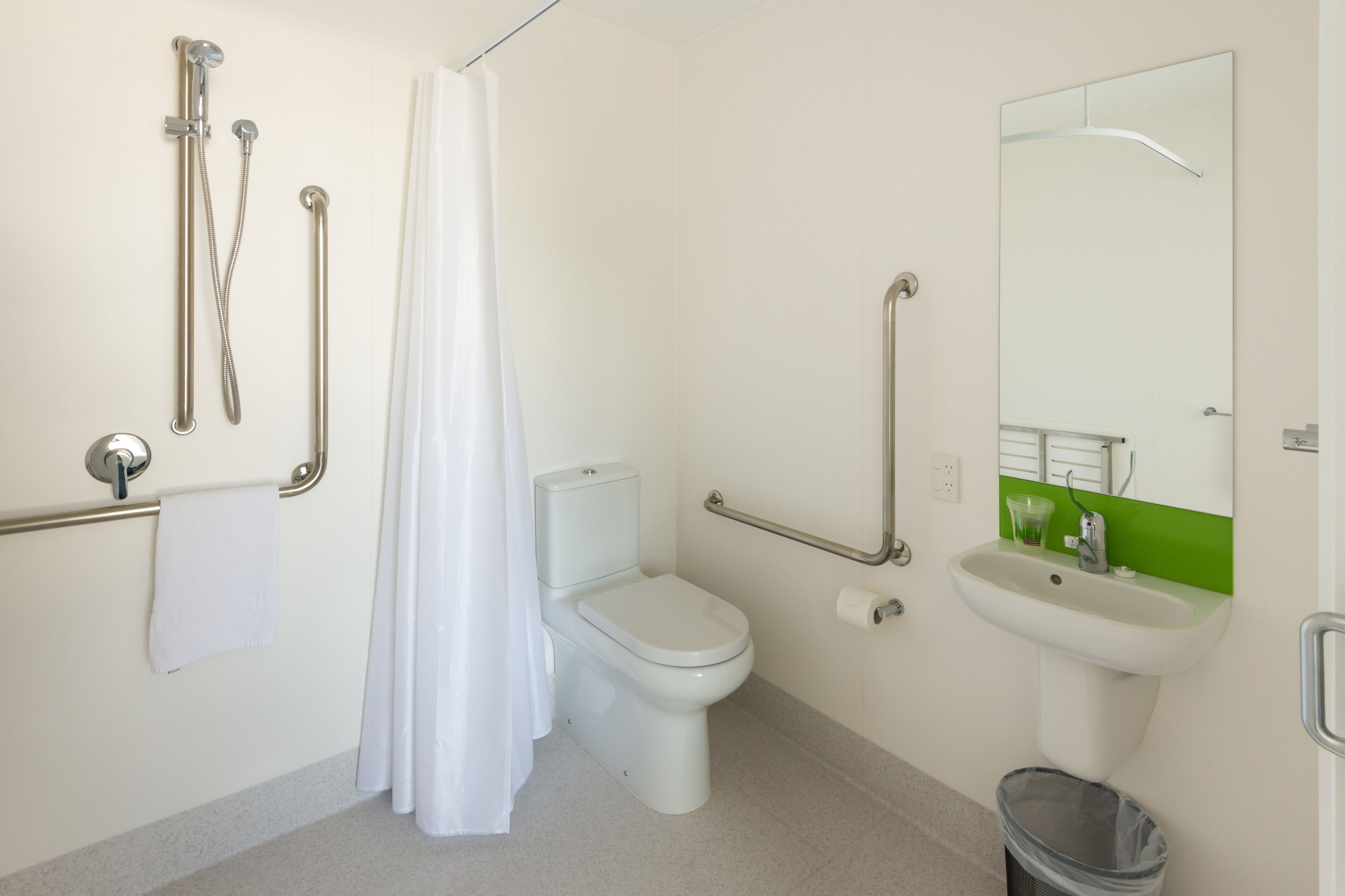 A bathroom with a toilet, a shower with grab bars, a sink, and a mirror.