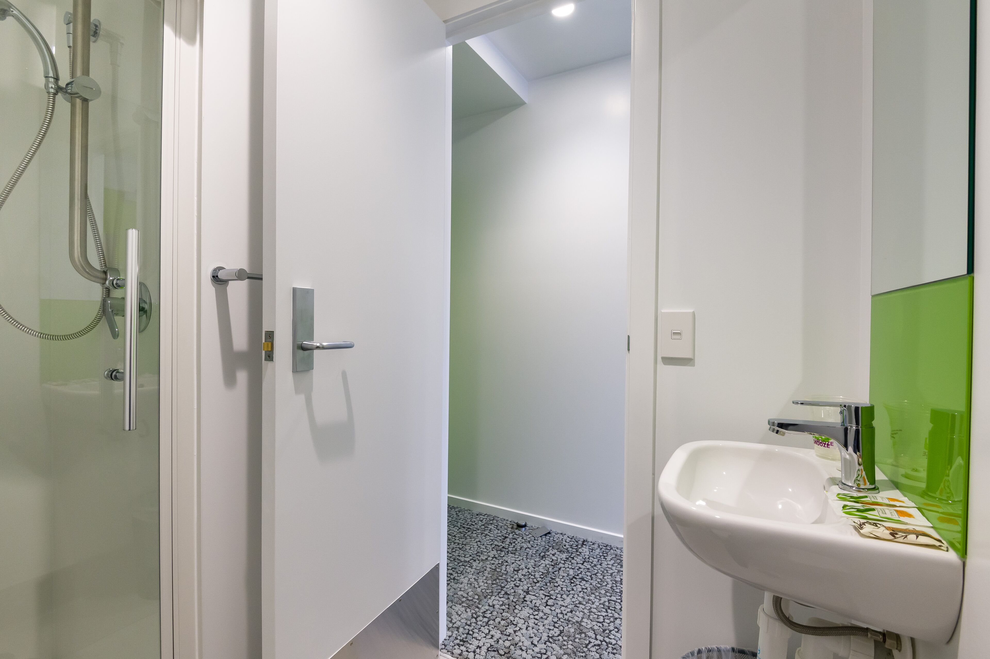 Ein modernes Badezimmer mit einer gläsernen Dusche, einem weißen Waschbecken und einem grünen Spiegel sowie einem gefliesten Boden.