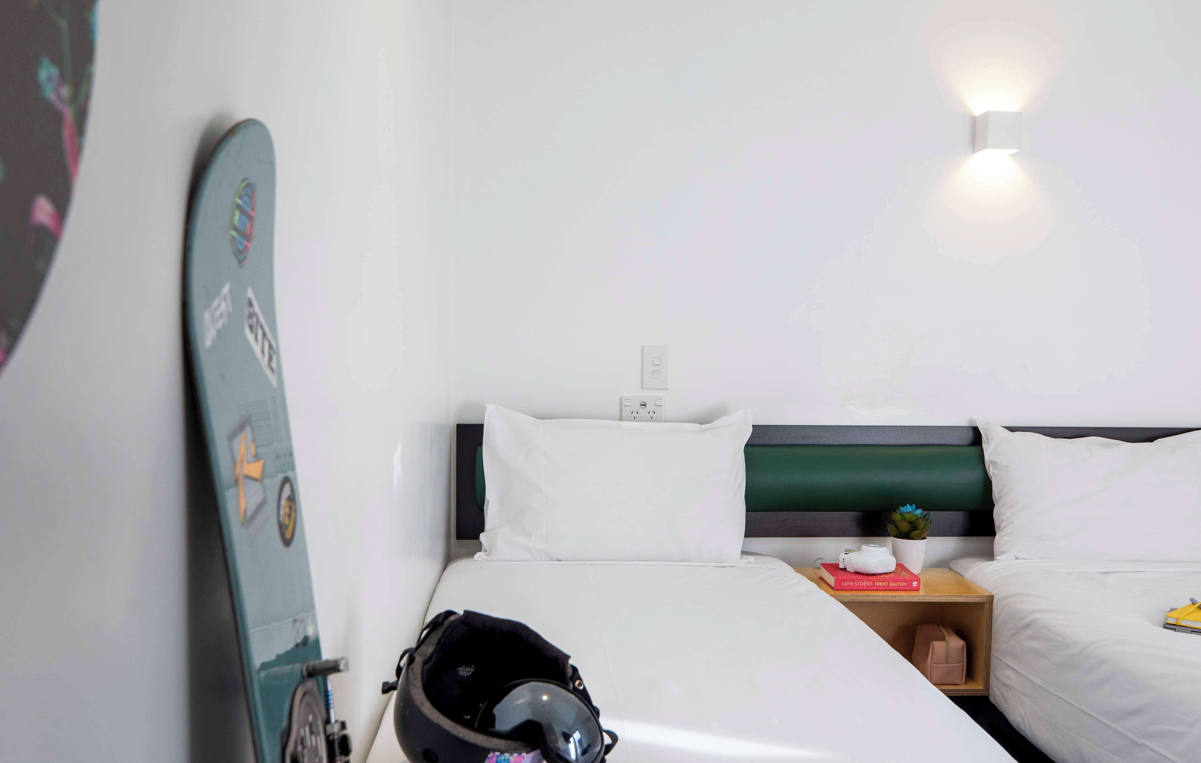 A hotel room with a bed, a nightstand, a surfboard, and a helmet.
