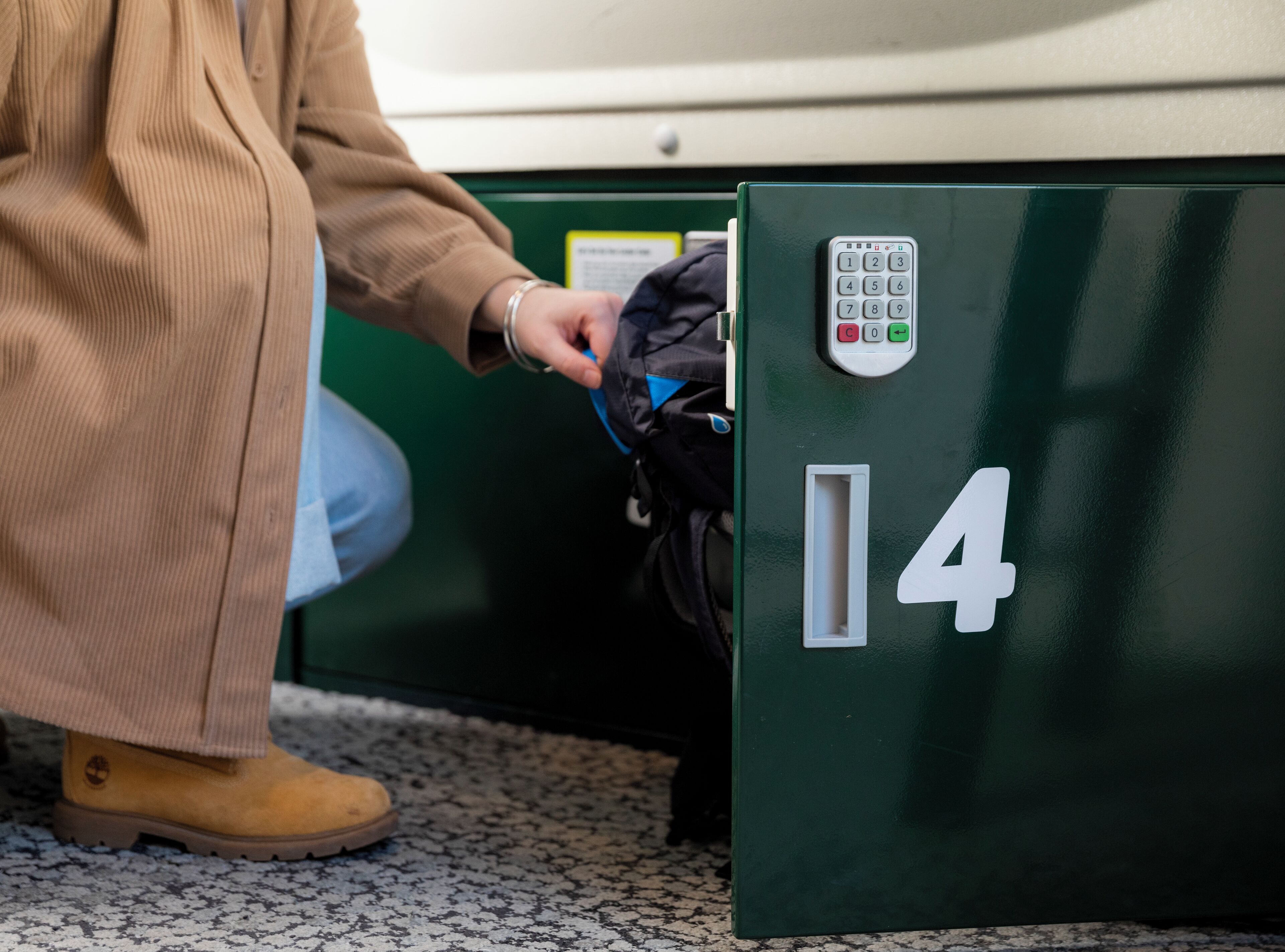 A person interacting with a green numbered box, possibly a mailbox or a locker.