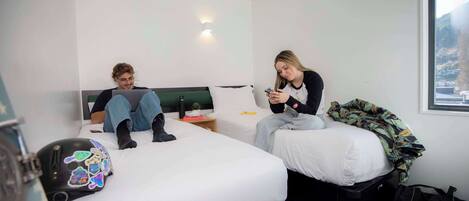 A hotel room with two beds, a nightstand, and a window with a view.