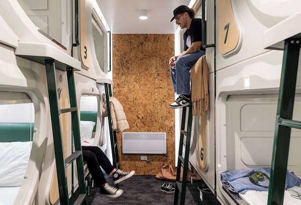 Compartimento de tren compacto con literas, un área pequeña para sentarse y una ventana.