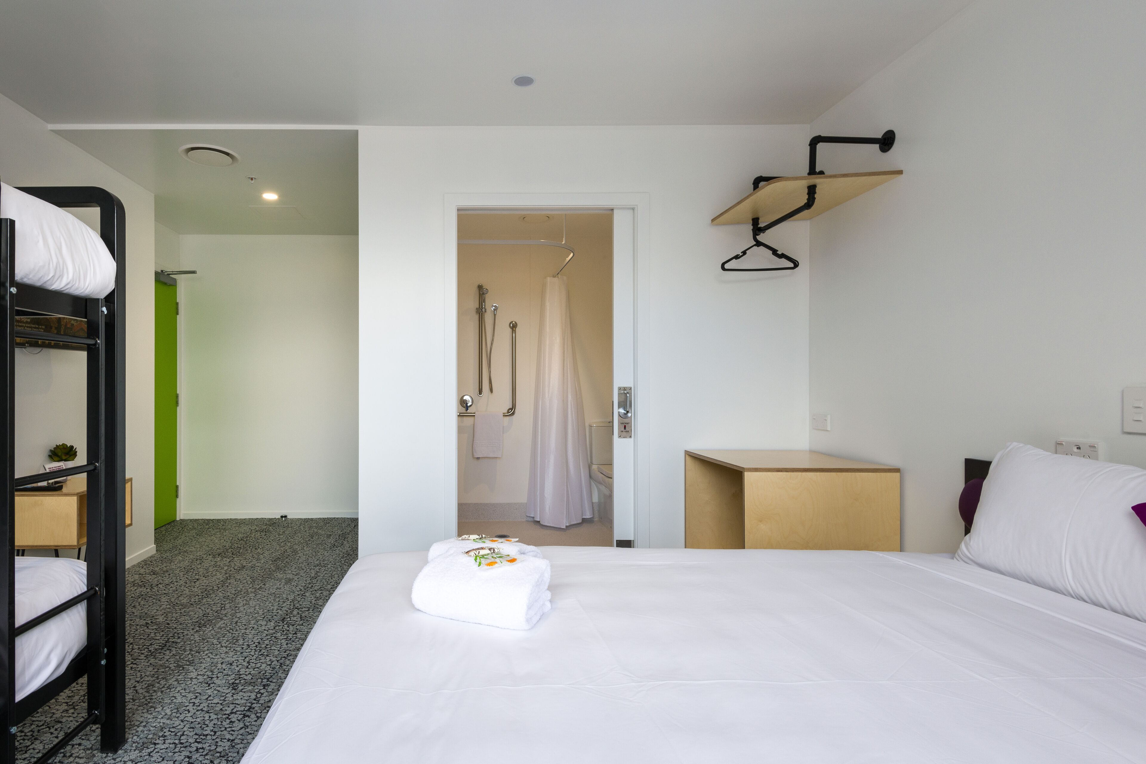 Habitación de hotel con literas, una cama individual, un escritorio pequeño y zona de ducha.