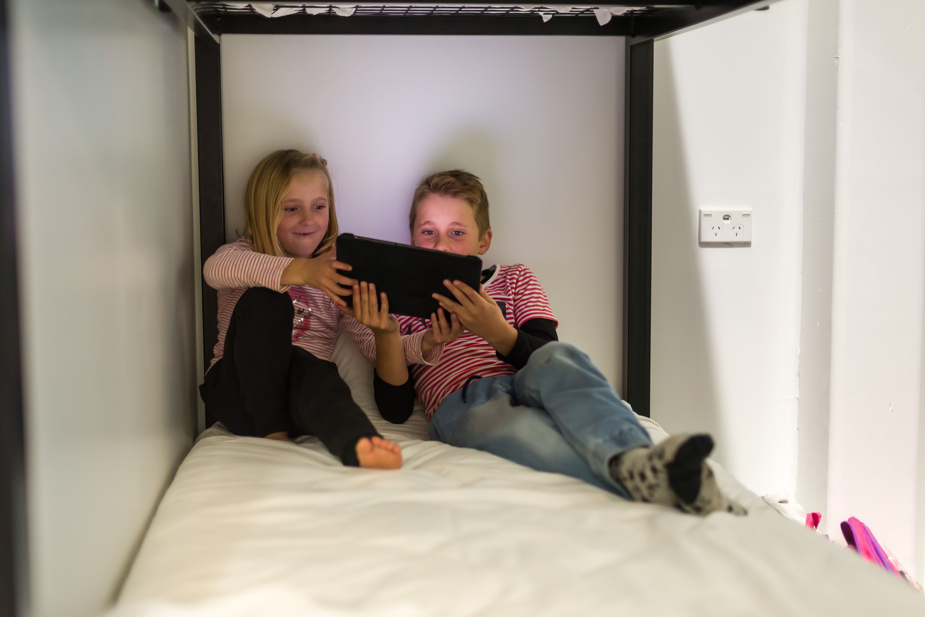 Two people lying on a bed in a room with white walls and a black frame.